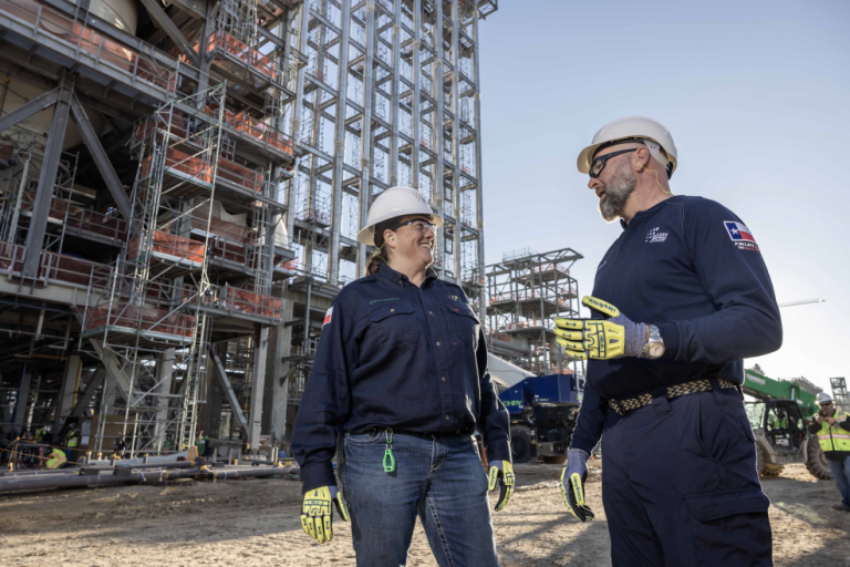 Two workers in foreground talking with plant in background